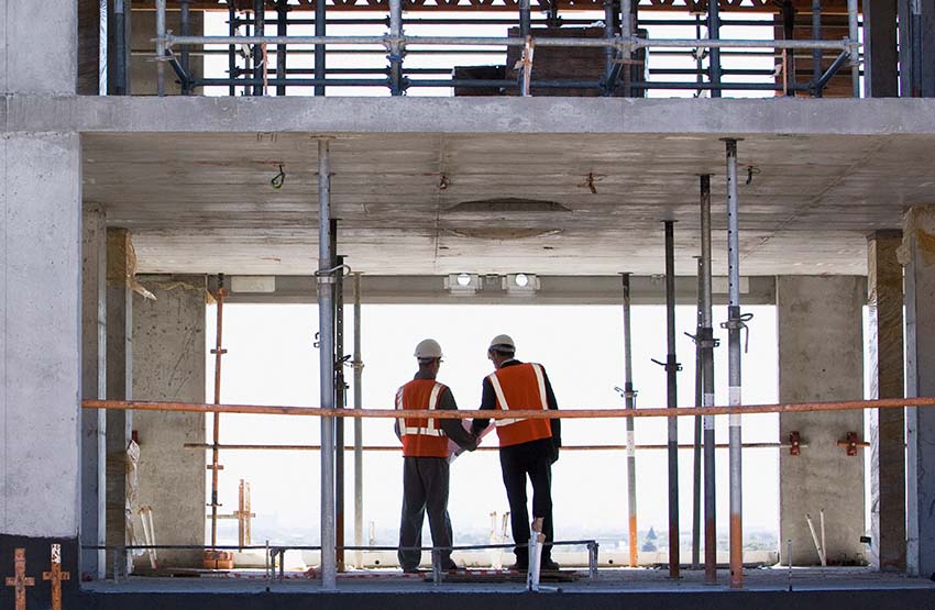 Two construction workers looking at blueprints together while at a construction site.
